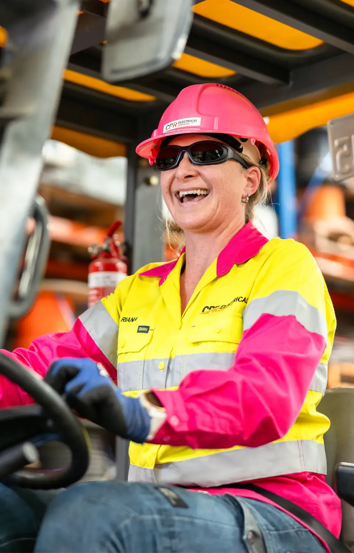 CPR Electrical worker in pink and yellow hi-vis and hard hat smiling at the controls of a forklift